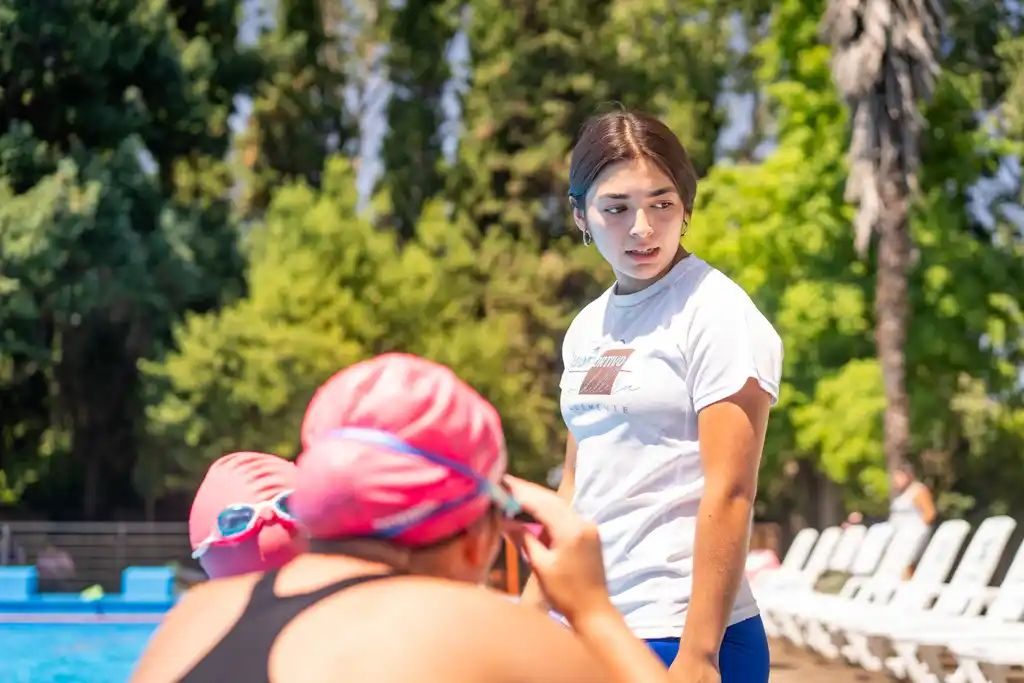 Profesora del club ayudando a una alumna a ajustar su gorro de natación