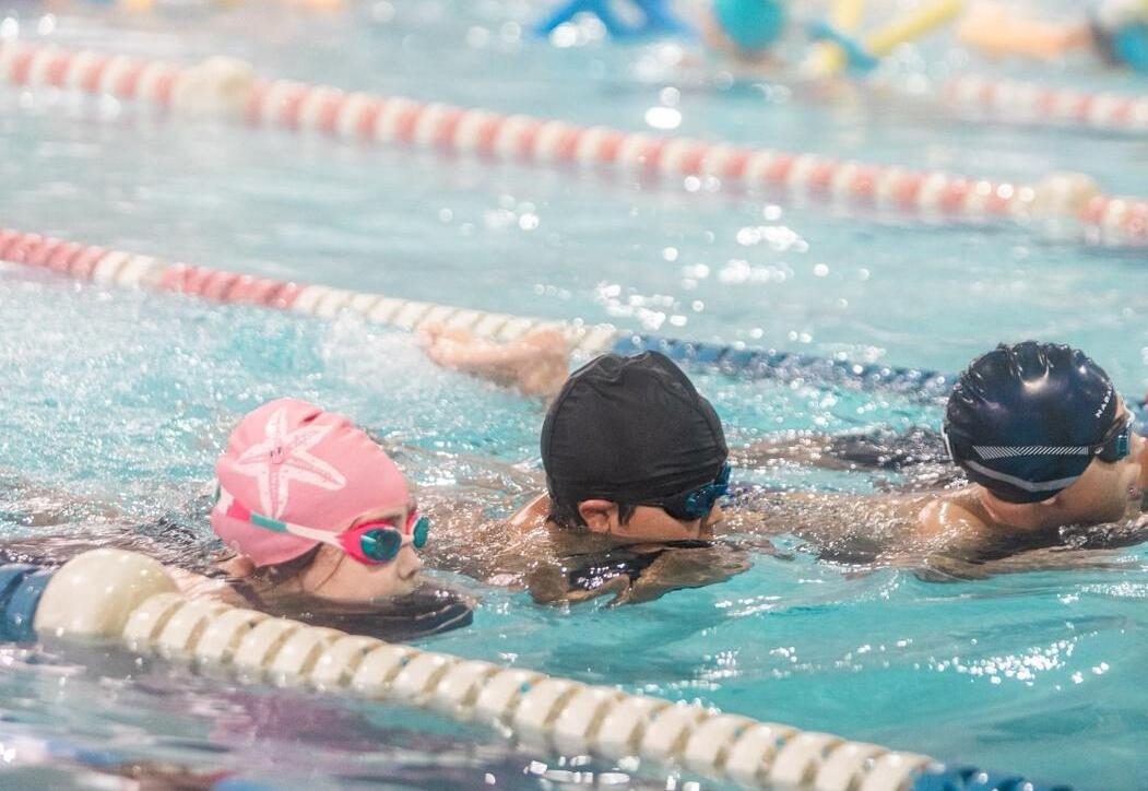 Tres niños nadando juntos durante una clase en la piscina temperada